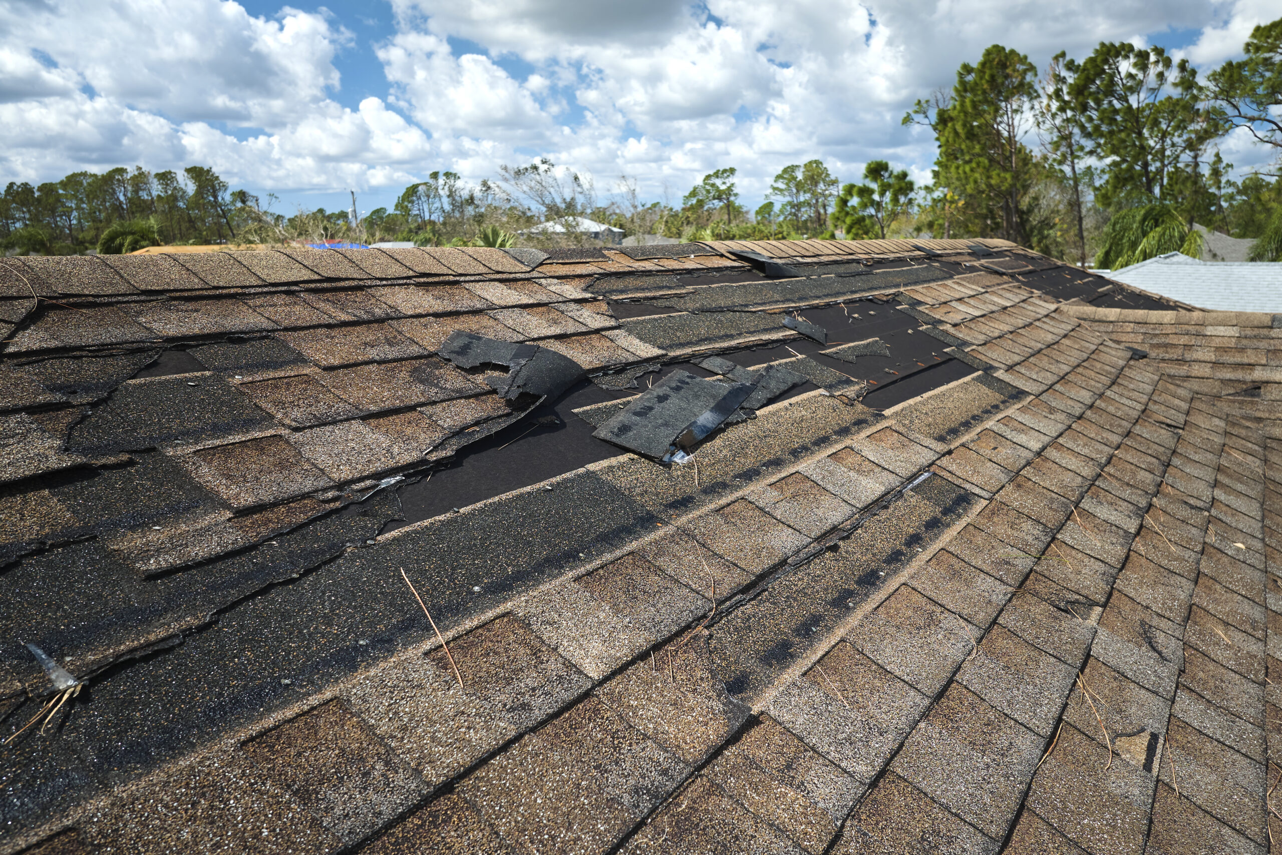 Damaged house roof with missing shingles after a storm.